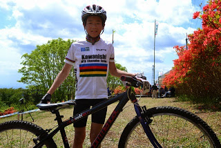 「Kawanishi」と書かれたスポーツウエアを着た長谷川連選手が、自分のマウンテンバイクと一緒にカメラの前でポーズをとっている写真