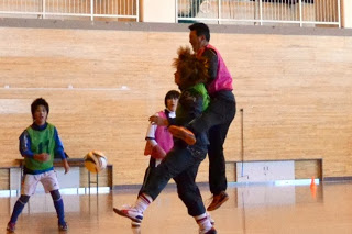 黄緑とピンクのビブスを着た選手がジャンプして競り合いながらボールを奪おうとしている瞬間の写真