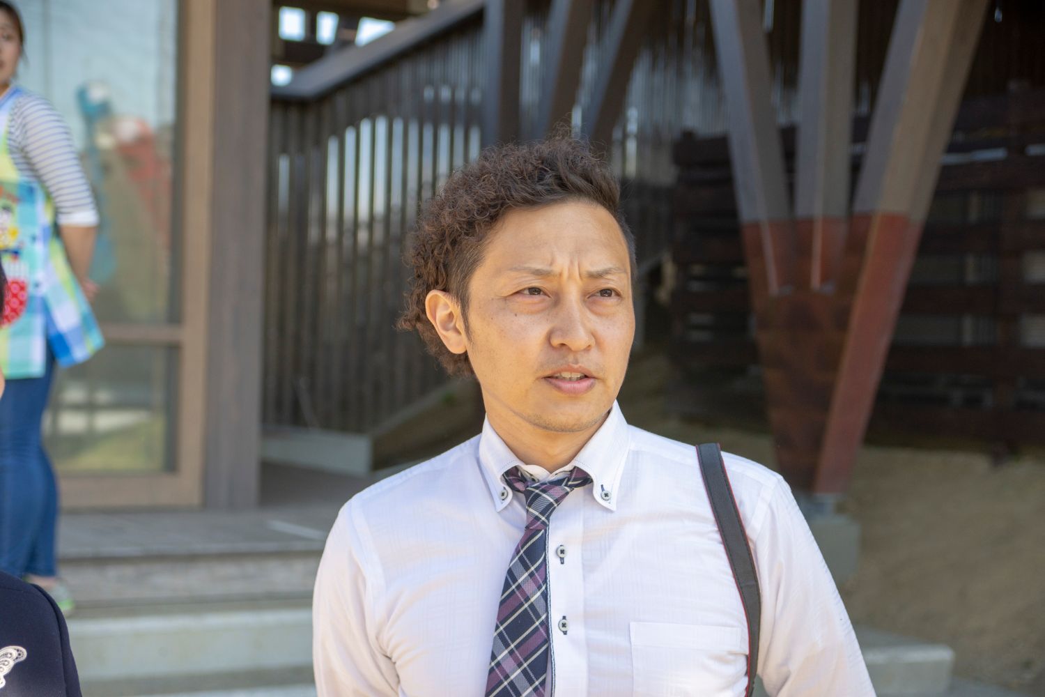 白いワイシャツにチェック柄のネクタイを締めた村松さんが、屋外に設置された鯉のぼりをまぶしそうに見ている様子をアップで撮影した写真