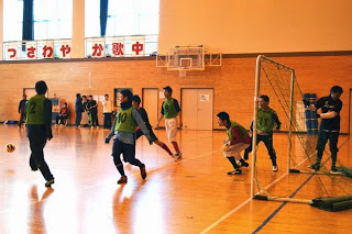 ゴール前で、緑のビブスの選手が複数でボールを追いかけ、守備と攻撃の動きがあるフットサルの試合中の写真