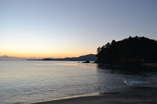 穏やかな波が打ち寄せる海岸沿いで、朝日が空と海をオレンジ色に染める静かな初日の出時の風景の写真