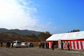 青空の下、広い敷地内に設置された紅白幕が飾られたテントの前で数人が集まっている様子を写した安全祈願祭の写真