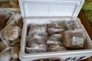 左側にはネット入りのニンニクが置かれ、白い発泡スチロールの中に複数のビニール袋に入った茶色い食品が収められている写真