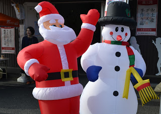 屋外に設置されたサンタクロースと雪だるまの空気で膨らませた人形が並んで立っている写真