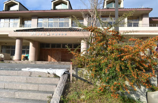 階段の上にある2階建ての明るいベージュ色の外観で正面玄関には太い柱が印象的な旧戸倉中学校の正面玄関を写した写真