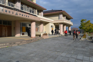 旧戸倉中学校校舎前の広場を複数の人々が歩いているのを正面玄関と校舎が写るように写した写真