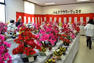 紅白幕の前に色とりどりのシルクフラワーが並び、来場者が鑑賞している展示会場全体の様子