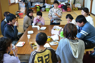 子どもたちと大人が和室に置かれた長机を囲んで座っており、お茶やお菓子を楽しみながら和やかに会話している様子を写した写真