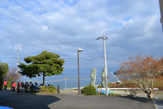 青空の下、モアイ像が2体置かれ近くに集まる見学者らしき人々の集団が海の方を見ている写真