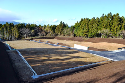 区画ごとに仕切られた平らな土地が山の中に階段状に並んでおり、中央に整備された道路とコンクリートの縁が見える整地済みの宅地の写真