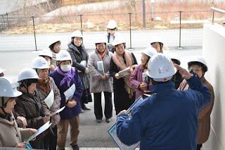 白いヘルメットをかぶった入谷婦人会の皆さんが資料を手に集まり、櫛田さんの話を聞いている写真