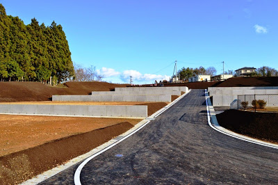 真ん中に舗装された道路が上へとまっすぐ続いている、複数の段差がついた土地がコンクリートの擁壁で仕切られた宅地造成地の写真