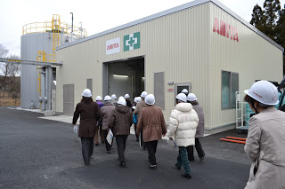 ベージュの壁の四角い建物の中に続々と入っていく入谷婦人会の皆さんの後ろ姿の写真