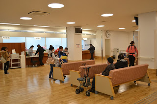 明るい室内にピンク色の背もたれの長椅子が3脚縦に並べて置かれている、受付前の待合スペースの写真