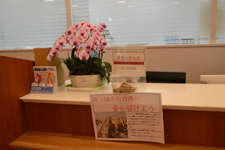 カウンターの上のピンク色の蘭の鉢植えの横に「南三陸から台湾へ愛を届けよう」とメッセージが添えられた募金箱が設置されている写真