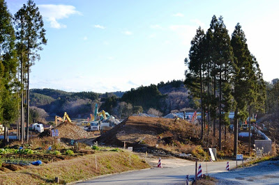 木々に囲まれた場所で多くの重機やトラックが入り、大規模な土地整備工事が進んでいる宅地開発中の現場の写真