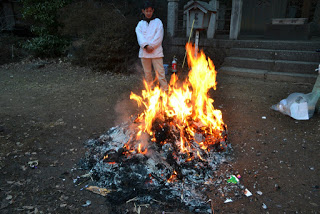 八幡宮の石段と拝殿がある境内で、お焚き上げが行われ大きく燃え上がる炎の前に白い服を着た男性が立ち見ている様子の写真