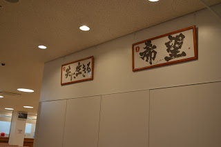 白い壁の天井付近に、茶色の額に入った、「共に生きる」「希望」と書かれた書が2つ並んで飾られている写真