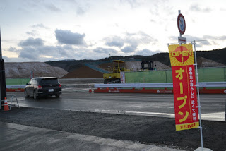 工事現場沿いの道路に面して、黄色と赤の配色の「オープン」と書かれたのぼりが立っている写真