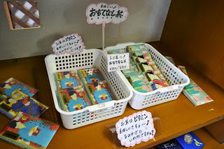 白いカゴに色鮮やかな絵柄がデザインされた紙パッケージのお茶が詰められ、「おもてなし茶」と書かれた手書きポップが添えられている写真