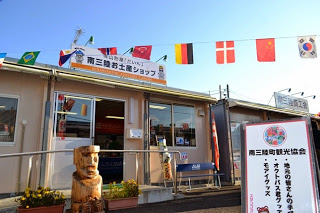 「南三陸お土産ショップ」と書かれた看板のあるプレハブ型の店舗入口に、木彫りの置物と案内看板が並ぶ写真