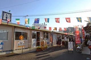 万国旗が頭上に飾られた仮設の建物が並び、多くの人が買い物をしている南三陸の仮設商店街のにぎやかな通りの写真