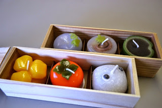 果物や和菓子の形をした精巧なつくりのカラフルなロウソクが3つずつ木箱に収めらた写真