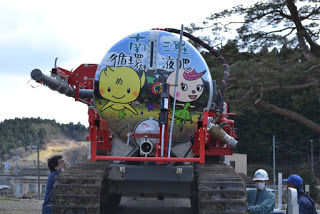 「南三陸循環液肥」の文字と黄色とピンク色のキャラクターが描かれた、液肥散布車のタンクを真後ろから撮影した写真