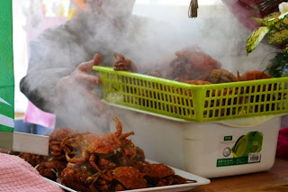 気が立ち上る中、蒸し籠から赤く茹で上がった蟹をプラスチックかごに移している様子が写されている写真