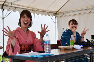 ピンクと青の着物を着た二人の女性が笑顔でポーズをとり、テーブルの席に座り楽しそうに過ごしている写真