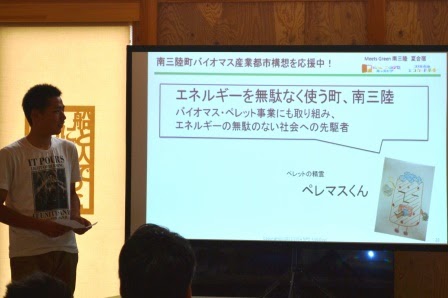 白いシャツを着た男性が「エネルギーを無駄なく使う町、南三陸」というテーマで、バイオマスペレット事業を取り組んでいる南三陸町について発表を行っている写真