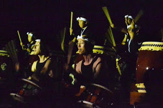 暗闇の中で額に鉢巻きを巻いた和太鼓の演奏者たちが、力強く太鼓を打ちながら真剣な表情を見せている写真