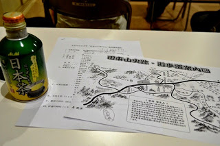 緑茶のペットボトルがある机の上に養成講座の資料と、「田束山史跡・遊歩道案内図」と題された手書き風の地図が置かれている写真