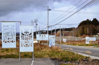 道路沿いに、白い切り絵模様が施された「きりこボード」が複数立てられ展示されている様子を写した写真