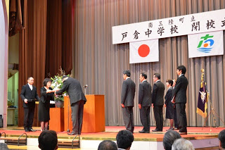 舞台上に「戸倉中学校閉校式」と書かれた横断幕と日の丸、南三陸町の町章が掲げられ、スーツ姿の関係者が整列する中で、壇上では感謝状のようなものが授与されている厳かな式典の様子を写した戸倉中学校閉校式の写真