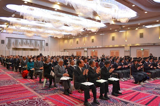 天井に設置されたシャンデリアが輝く大きなホールで、大勢の先生方や全校生徒が着席し拍手をしている様子の写真