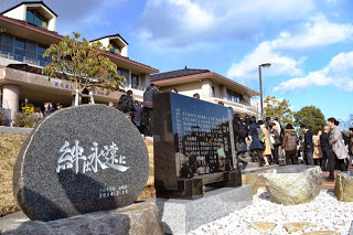 大勢の卒業生や在校生が集まる校舎の前に、「絆よ永遠に」と刻まれた石碑と黒い石碑が並んでいる様子の写真
