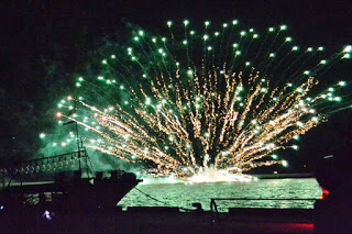 水面の近くから扇のように広がった緑色の花火が水面を照らし、観客席からもその美しさが見渡せる写真