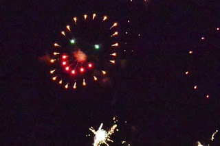 夜空に目が緑色で赤の光で描かれたニコニコ顔の花火が打ち上がり、笑顔の形がはっきり見える写真