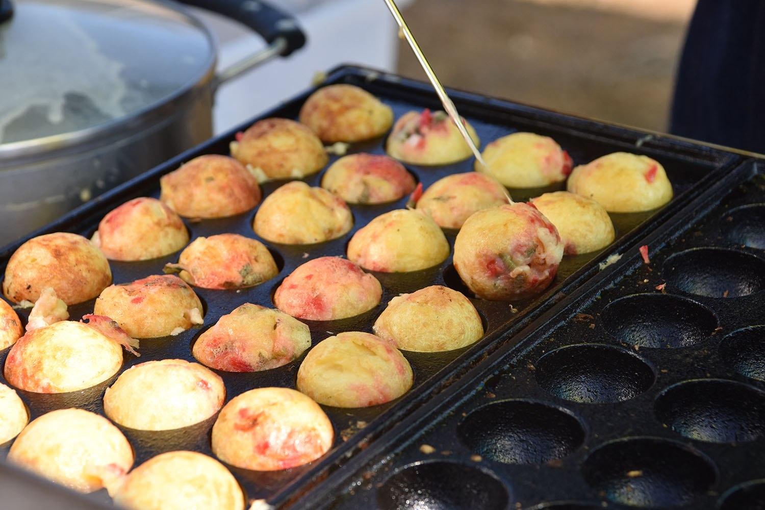 鉄板に丸く焼き上がったたこ焼きが沢山並んでいて、一本の串で一つをひっくり返そうとしている様子の写真