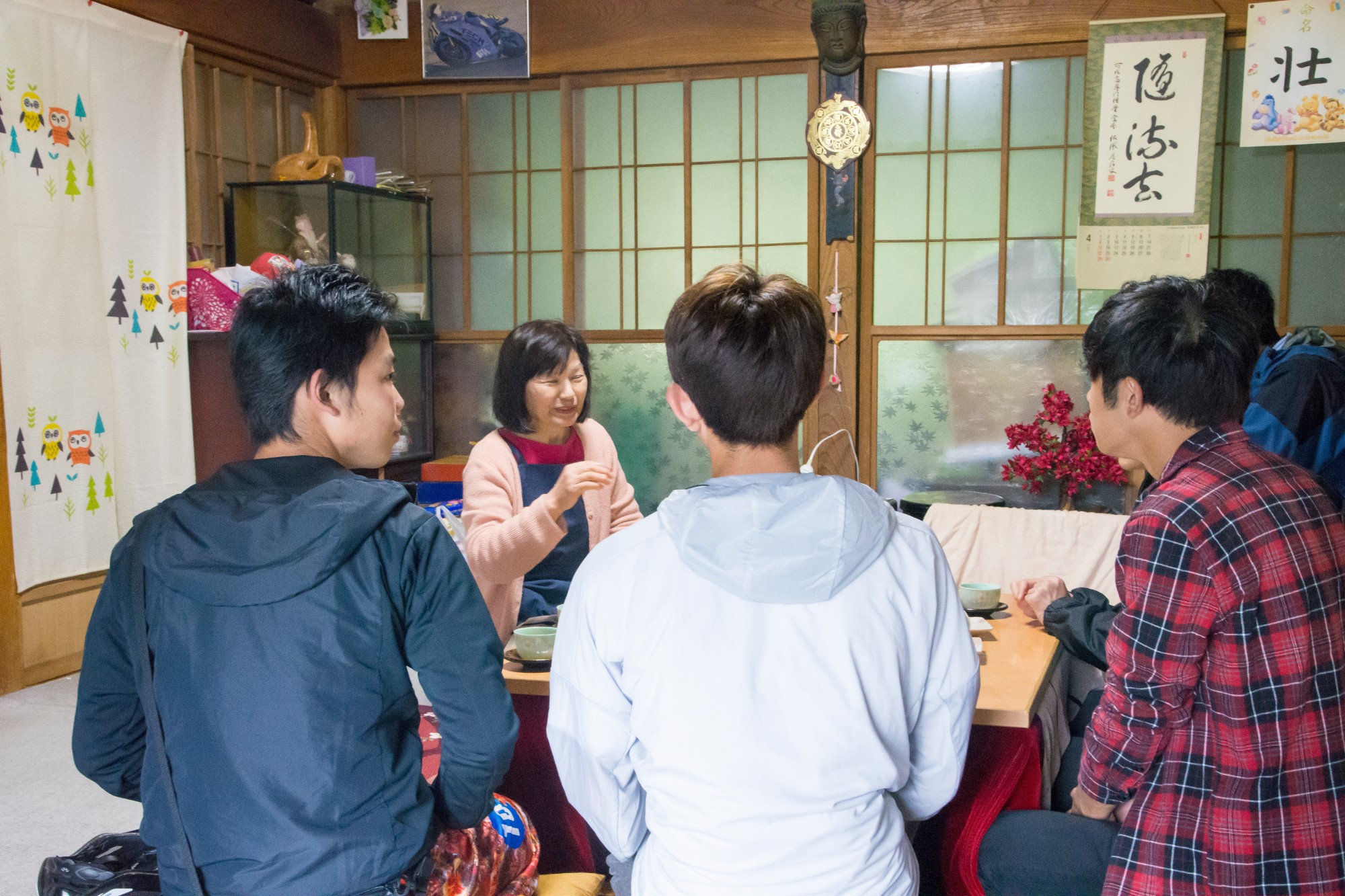 和室の居間で女性が中央に座り、対面に座った4人の男性たちとお茶を飲みながら楽しそうに話をしている、お茶っこの様子の写真