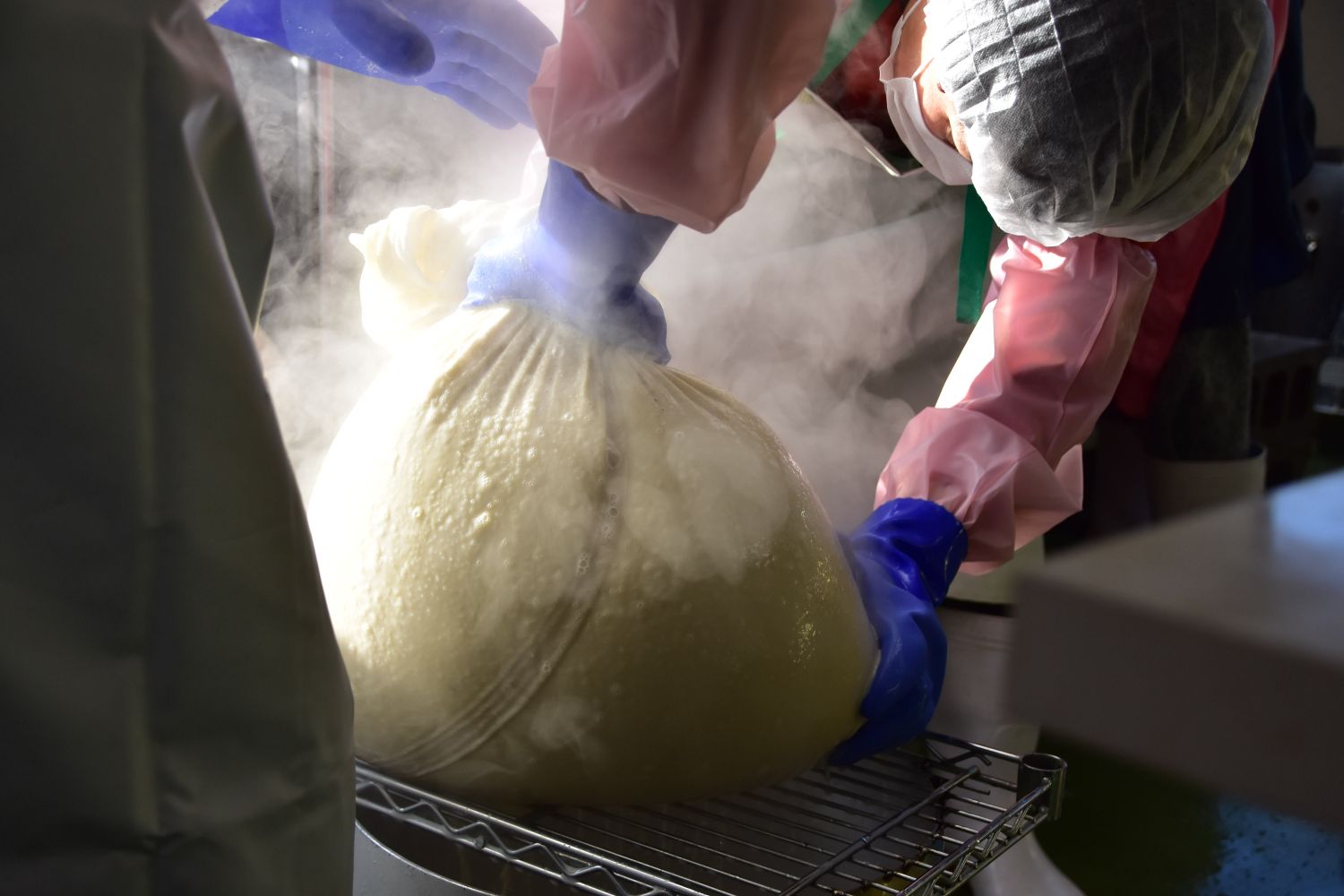 鍋で煮た豆を大きな袋に入れ煮汁を絞っている様子の写真