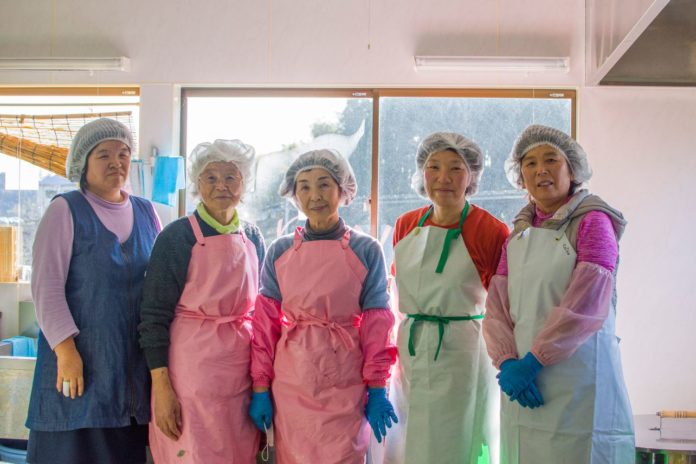 頭に不織布キャップをつけエプロンを着用した5人の女性が横一列に並んでいる写真