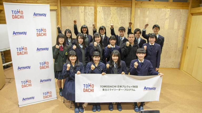 「TOMODACHI 日本アムウェイ財団 東北ミライリーダー・プログラム」と書かれた横断幕を持った生徒たちが3列に並び、1列目と2列目の生徒はガッツポーズ、3列目の生徒は拳を握った手を上げている集合写真