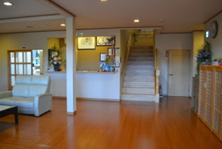 白いソファと木の床が特徴的なロビーの中央に、受付カウンターと階段が見える宿の玄関ホールの写真