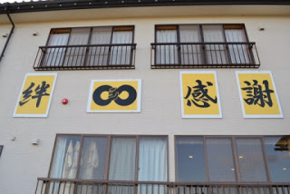 宿の外壁に「絆」「∞(無限)」「感謝」と書かれた黄色い看板が並んで掲げられている写真