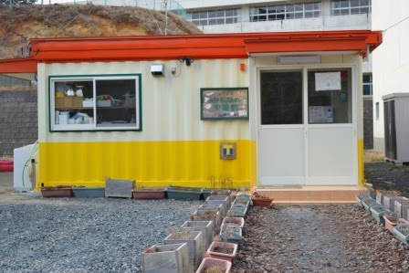 ガラスの引き戸があり、赤い屋根で上半分が白、下半分が黄色のコンテナハウスの建物外観の写真