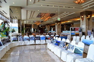 南三陸ホテル観洋のチャペルに白いカバーがつけられた椅子がたくさん並べられ、椅子の上に写真パネルが展示されている写真展の様子の写真