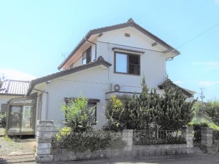 家の周囲に塀と植木がある白い外壁と茶色い瓦屋根を持つ二階建て住宅の写真