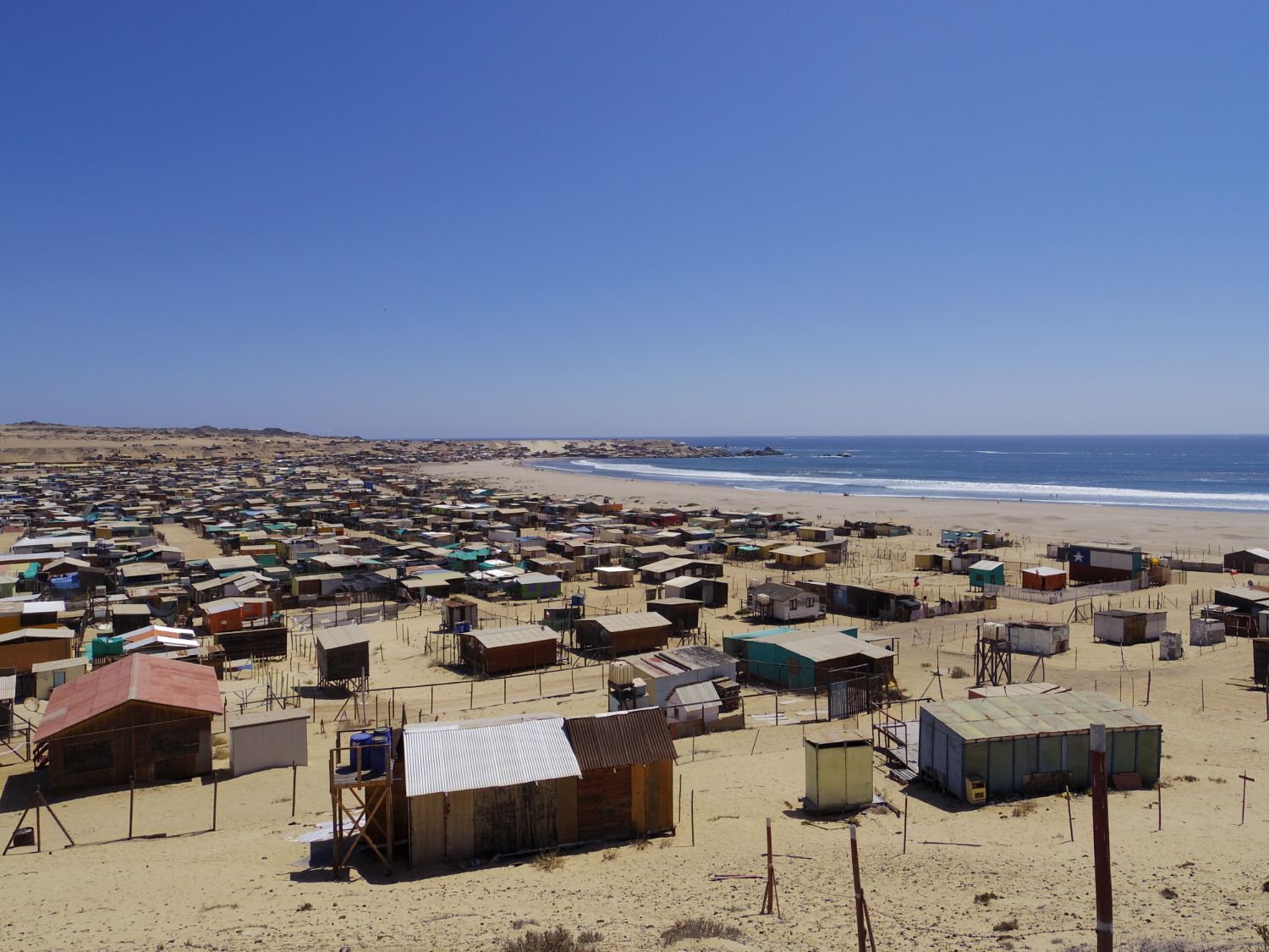 海に面した砂漠のような土地に数百軒の木造の簡易的な家が広がっている写真